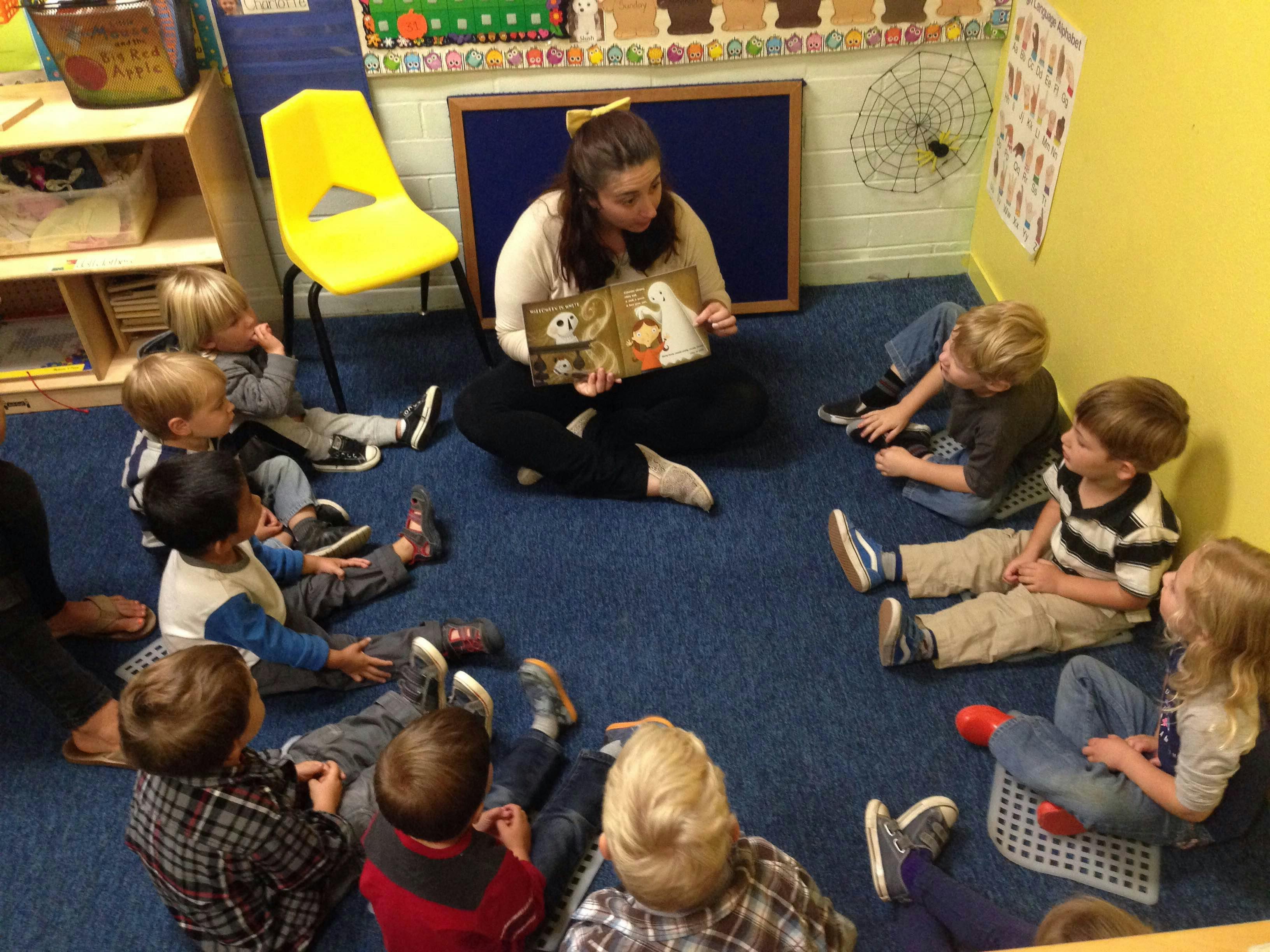 Person reading a book to a group of children sitting on the floor