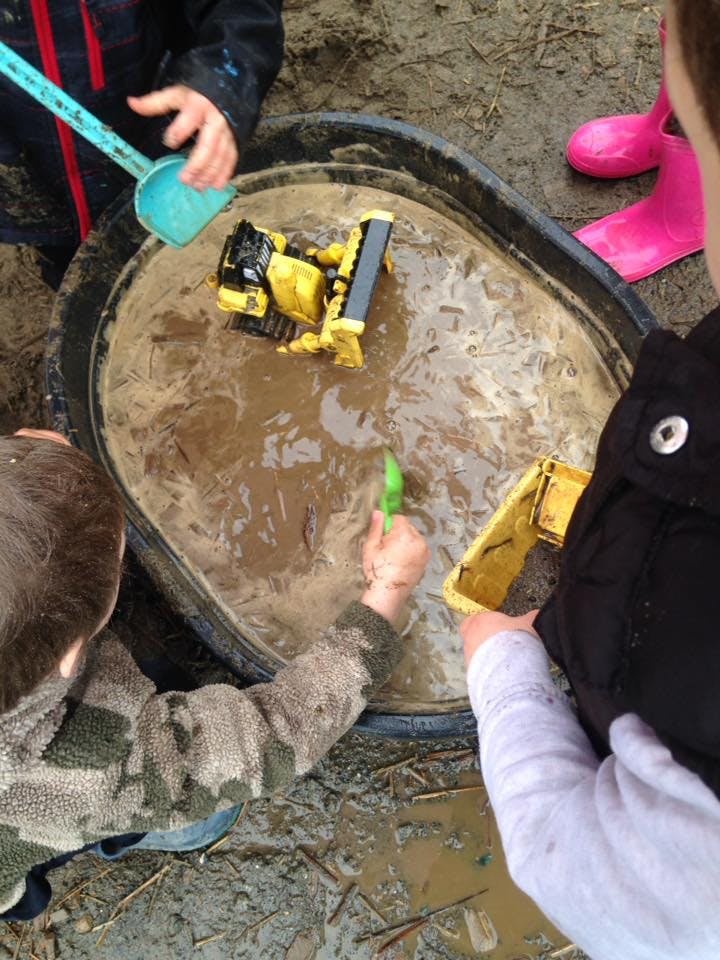 Children playing with toy construction vehicles in a tub of mud