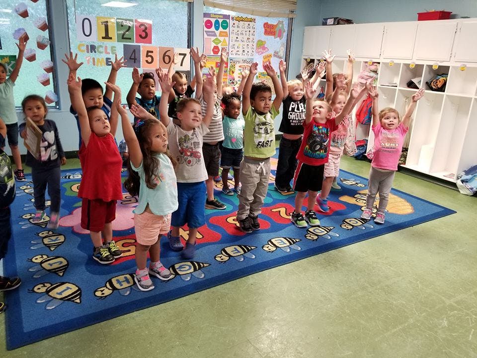 Group of children standing on a rug with their arms raised in a classroom