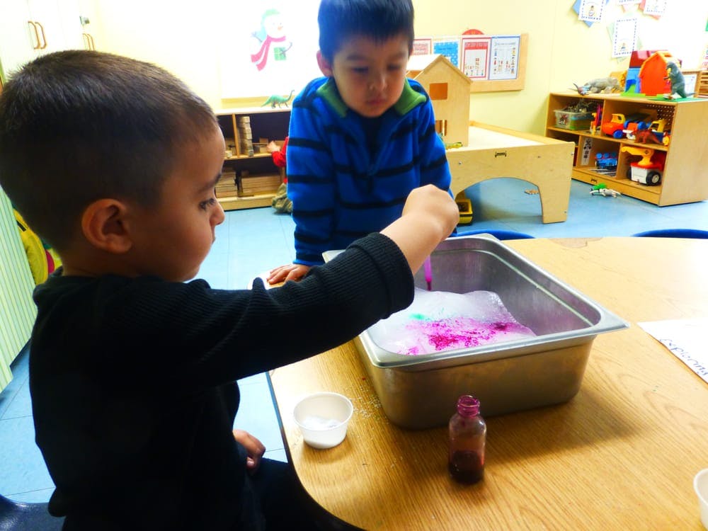 Two children playing with bubbles and colored liquid in a classroom