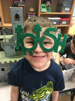 Child wearing green glitter glasses that spell "Irish"