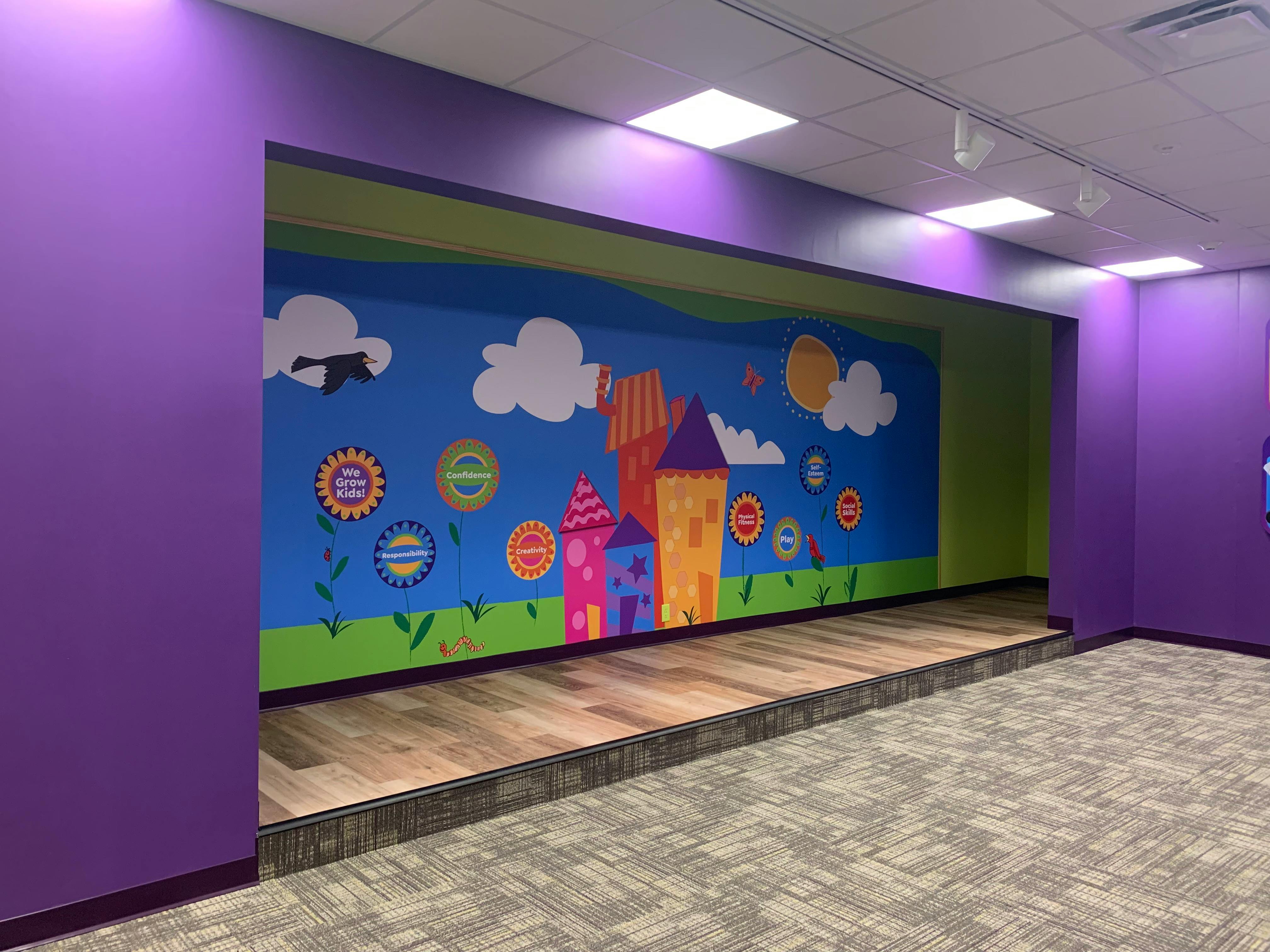 Children's room with purple walls, a stage, and a mural depicting colorful houses and flowers