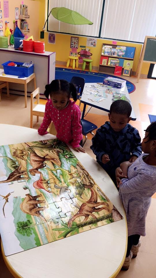 Three children looking at a dinosaur puzzle on a table in a classroom