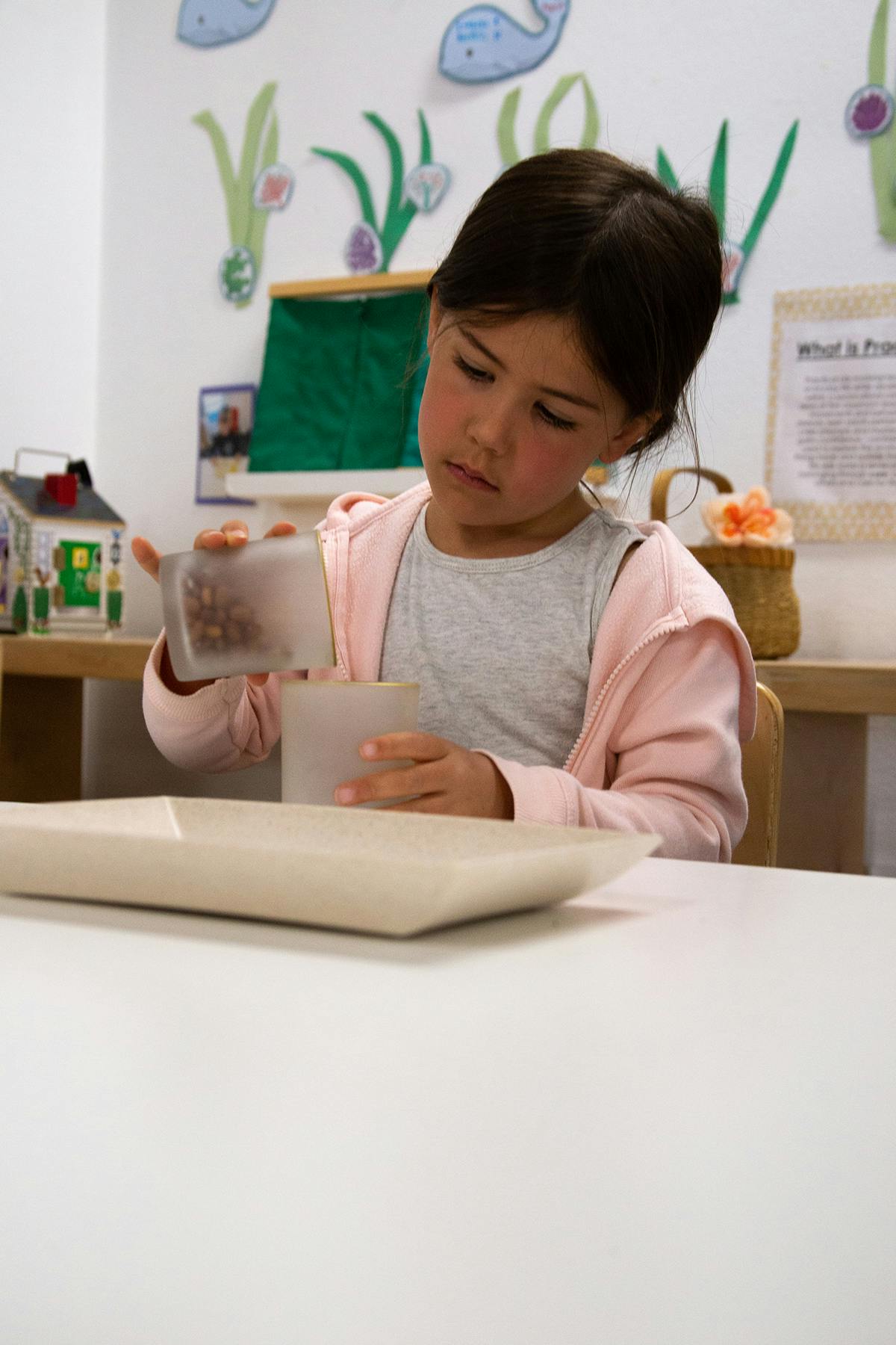 Child pouring from one container to another at a table