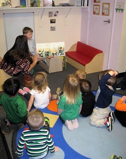 Adult reading a book to a group of children in a classroom