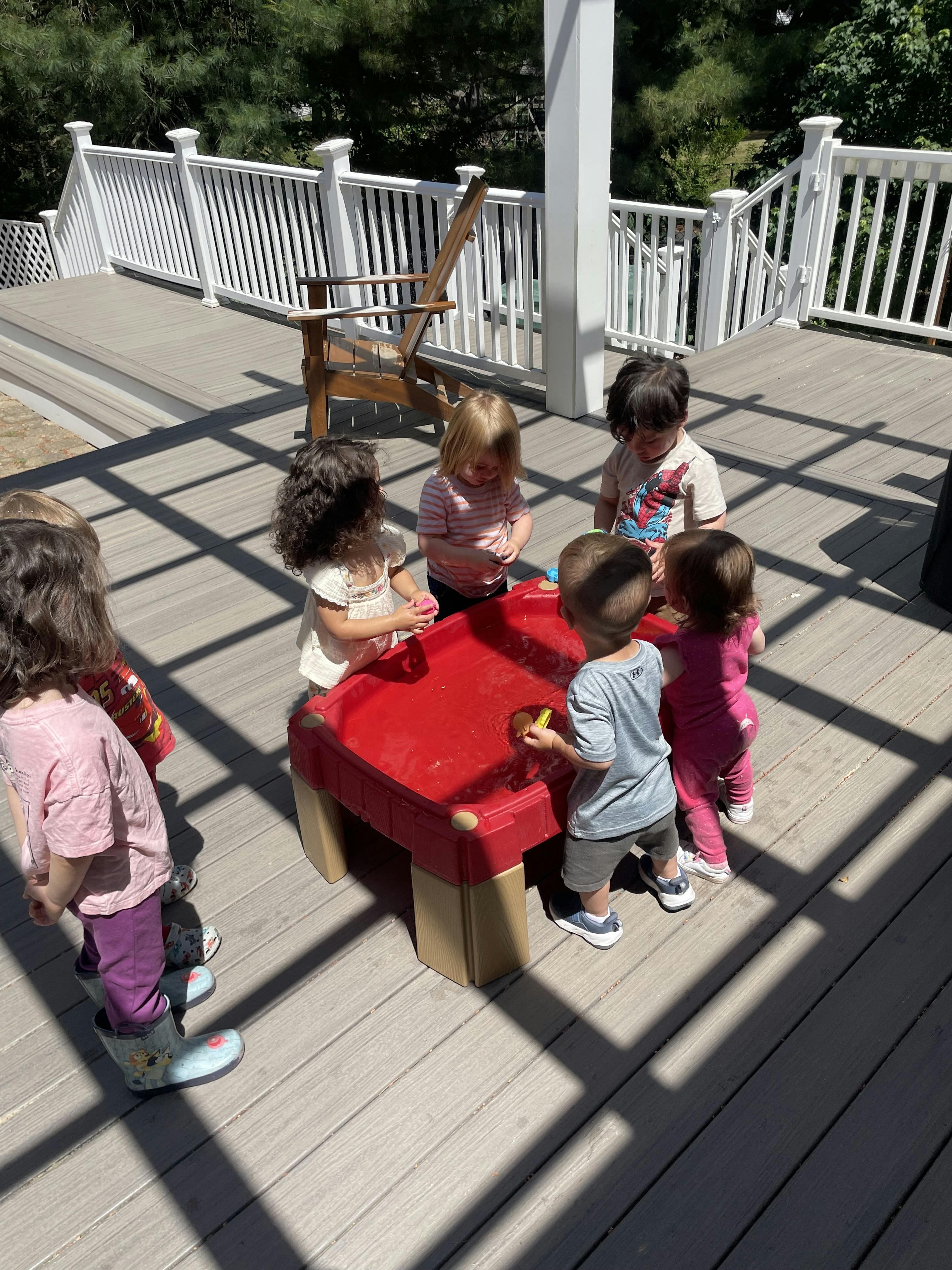 Group of children playing at a red water table on a wooden deck