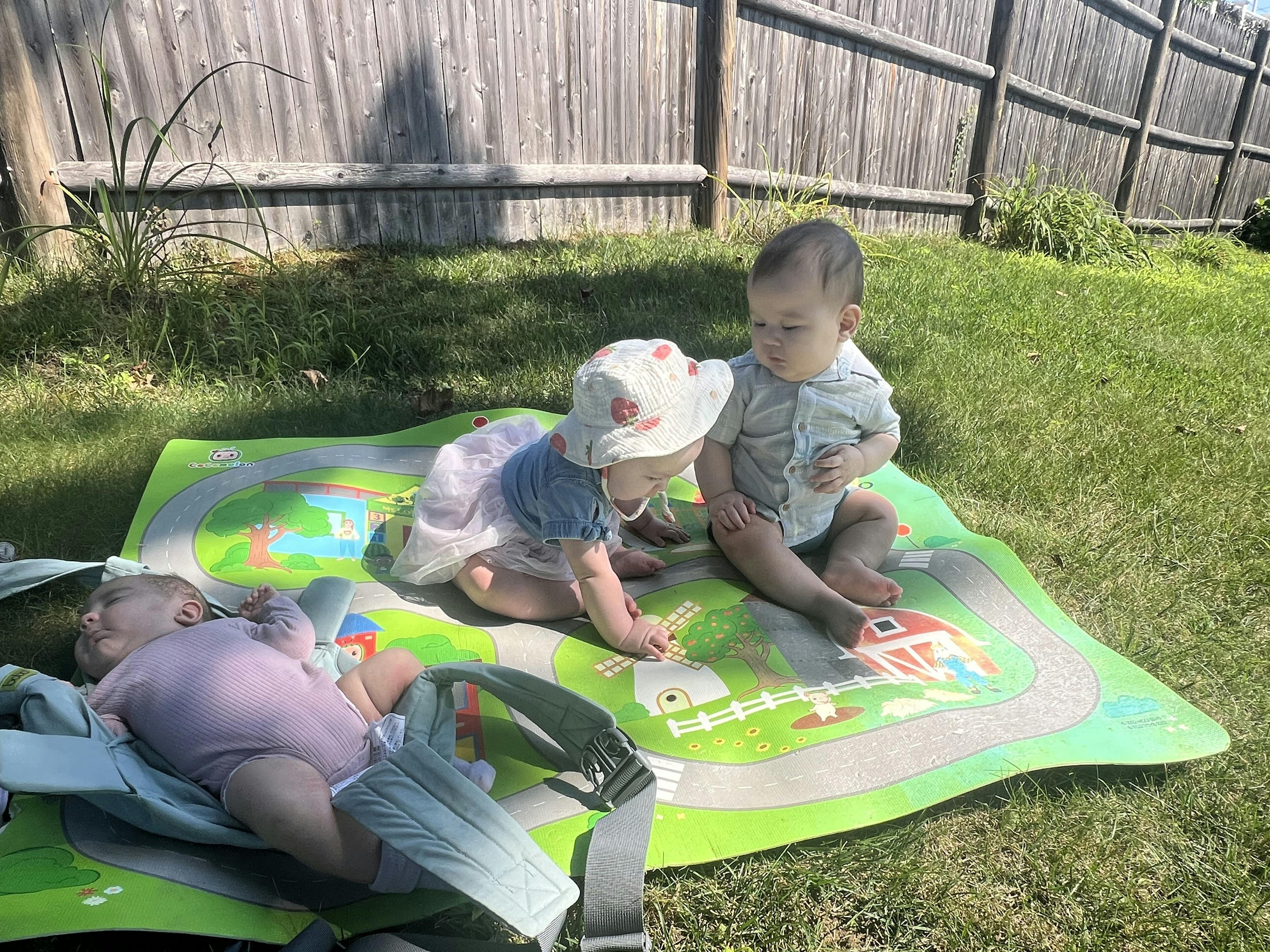Three children playing on a mat in a grassy yard
