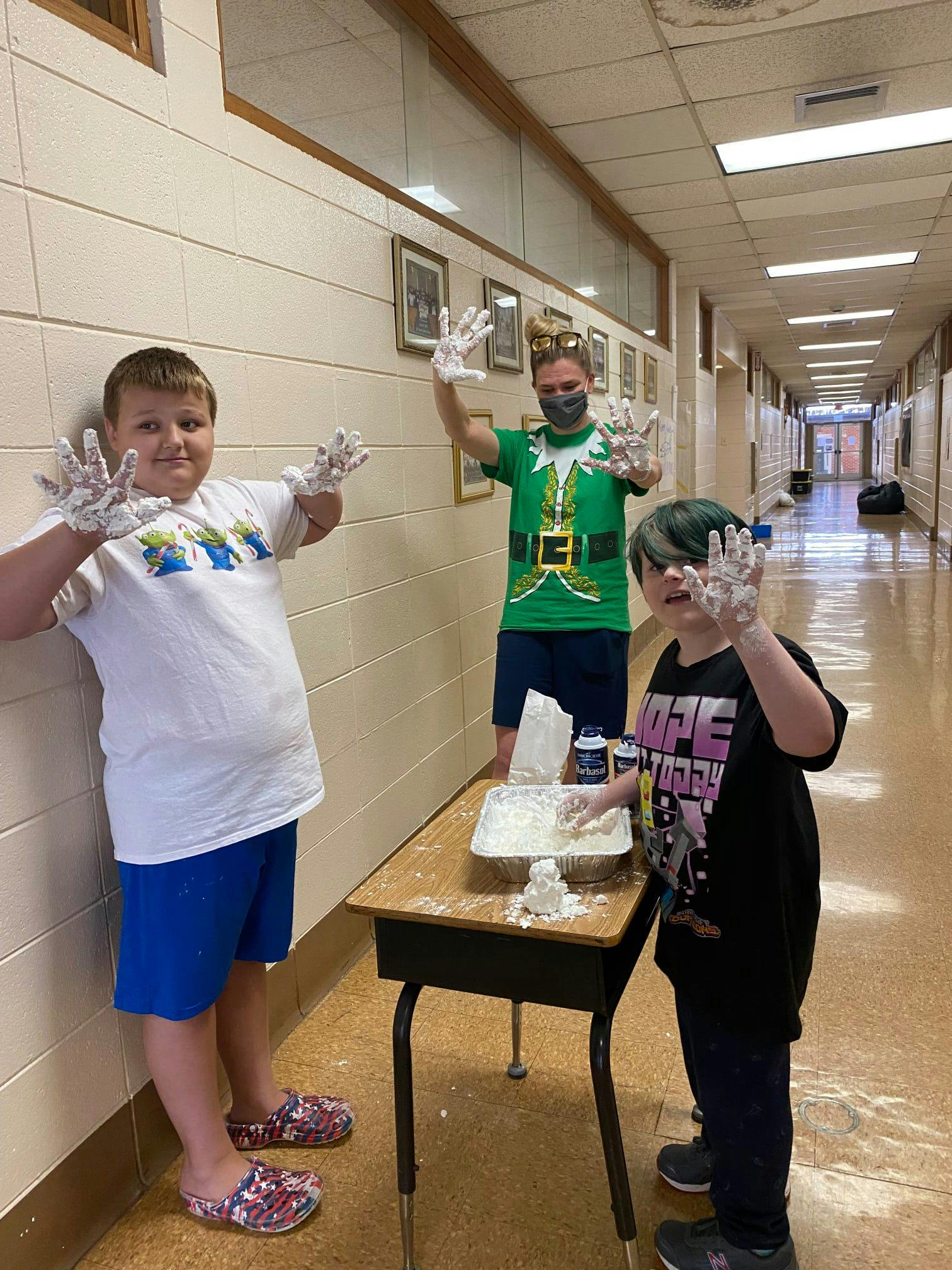Three children with white powder on their hands, one standing at a desk