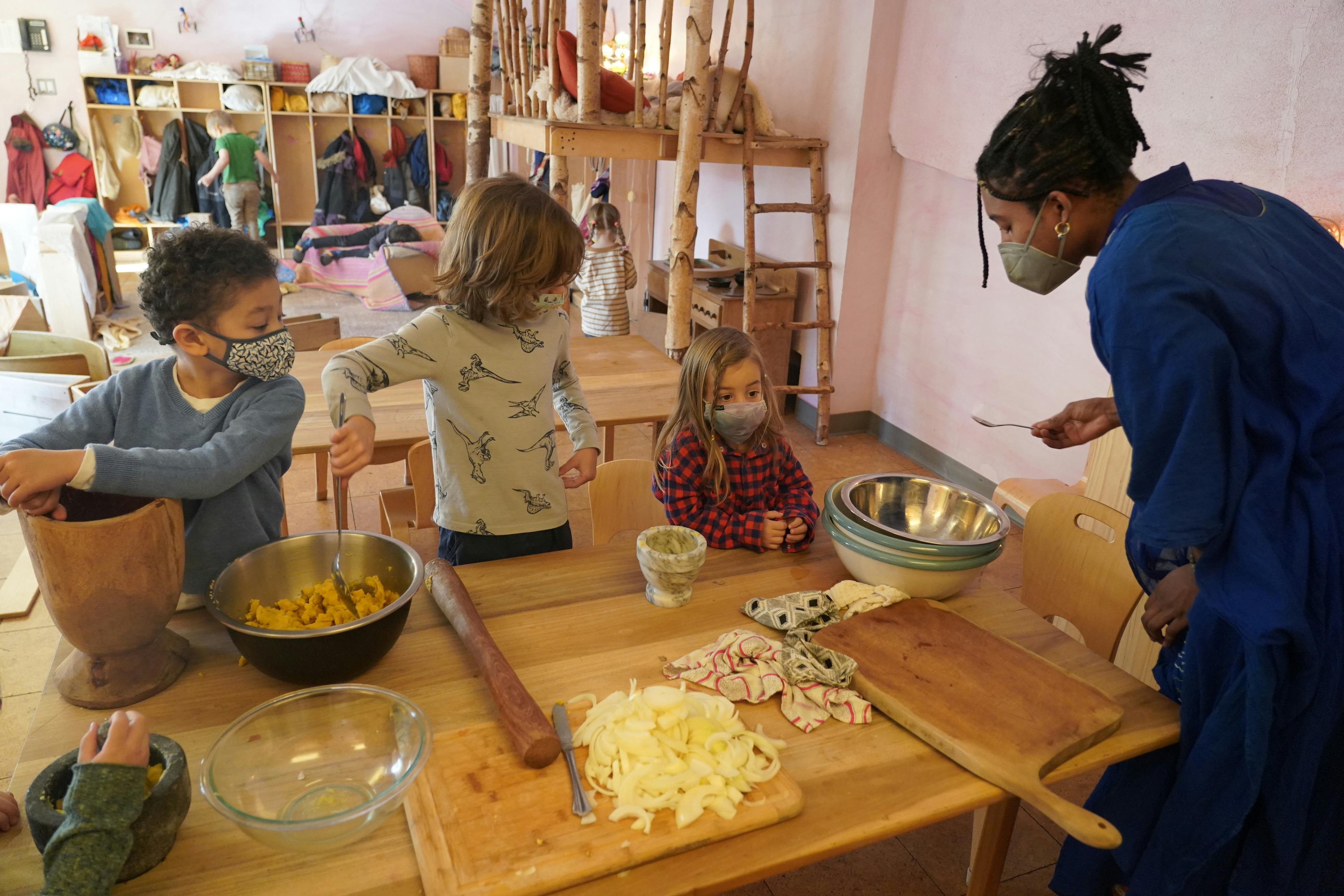 Adult and children in masks preparing food at a table