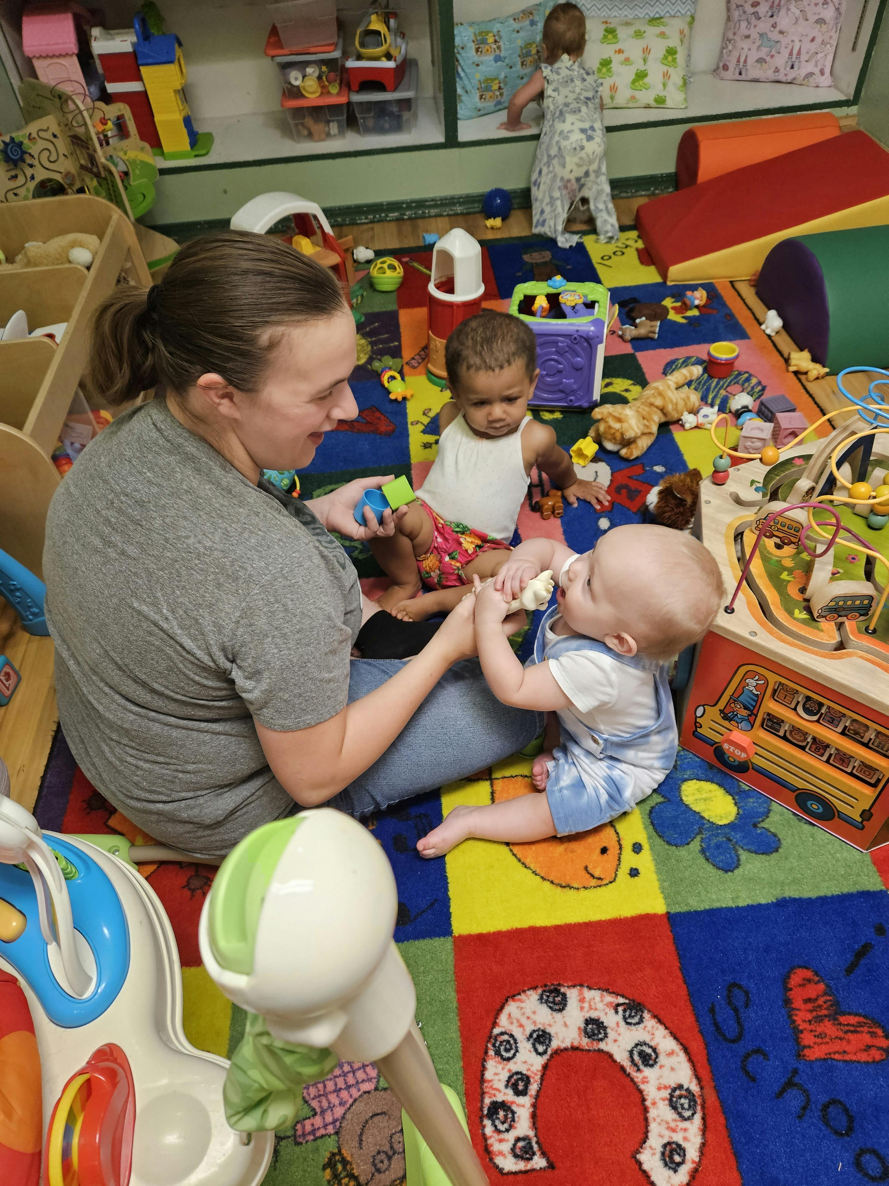 Person sitting on floor with two babies in a play area