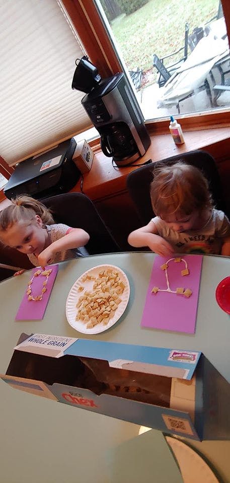 Two children doing a craft with cereal pieces on purple paper