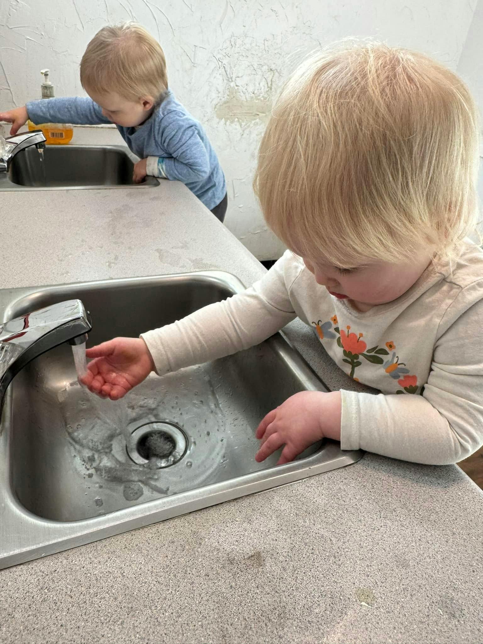 Two children playing with water in sinks