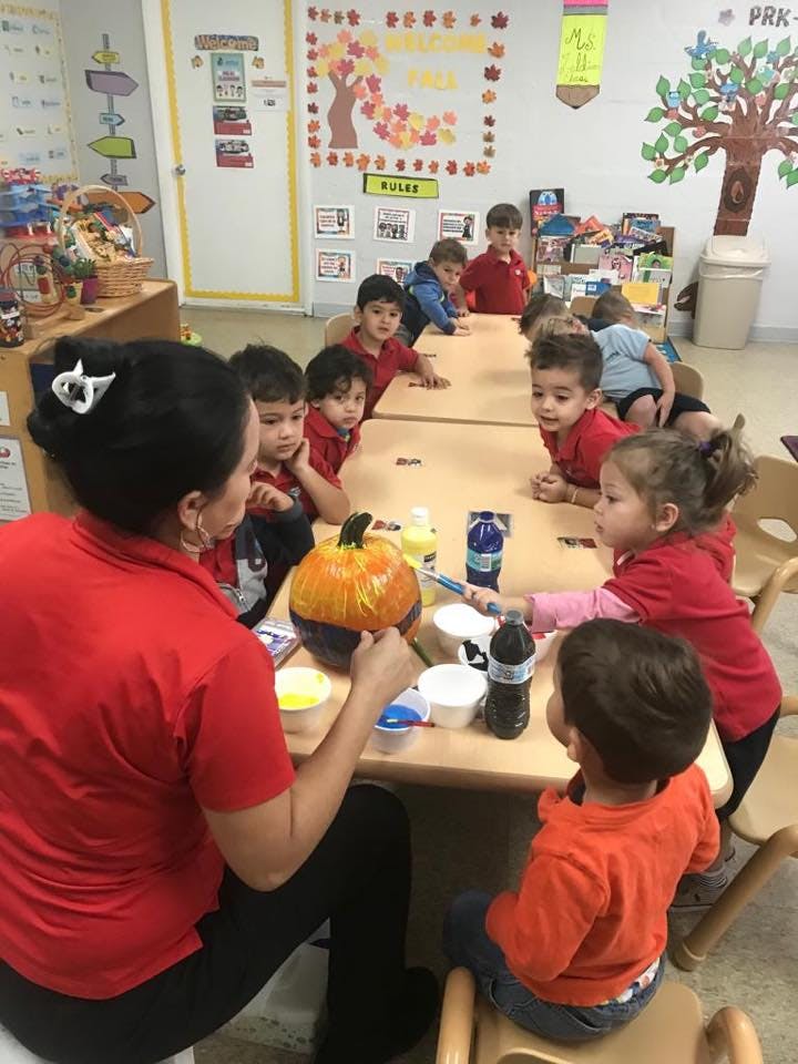 Adult and children painting pumpkins at a table in a classroom