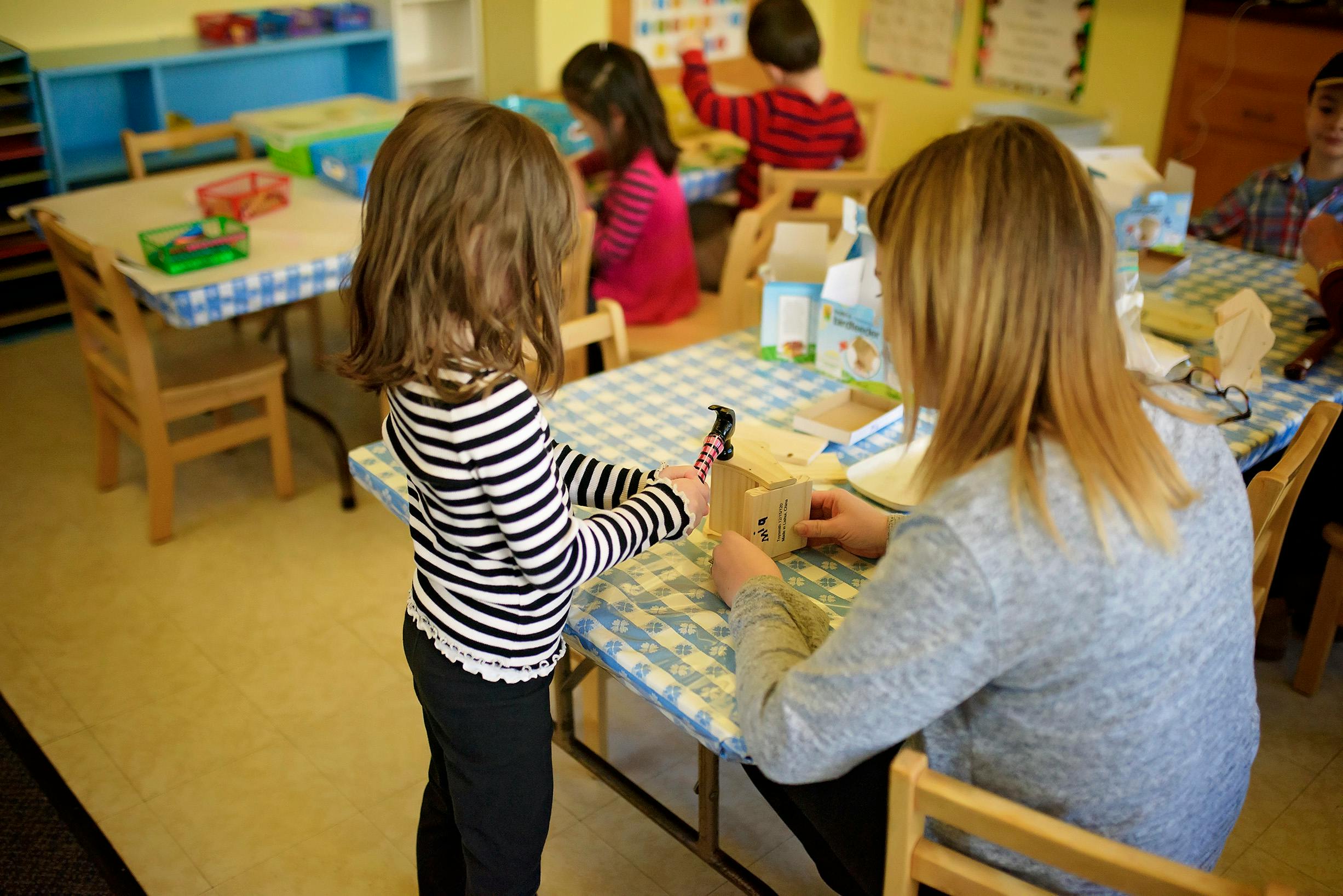 Child standing at a table with an adult in a classroom