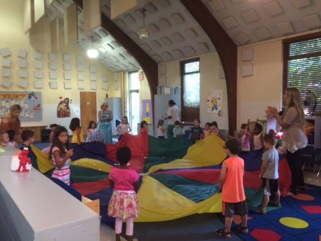 Children and adults playing with a colorful parachute in a classroom