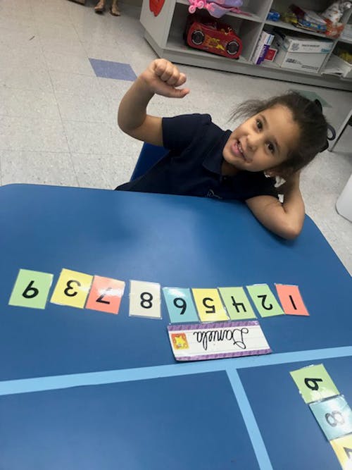 Child sitting at a table with number cards, letter, and name cards