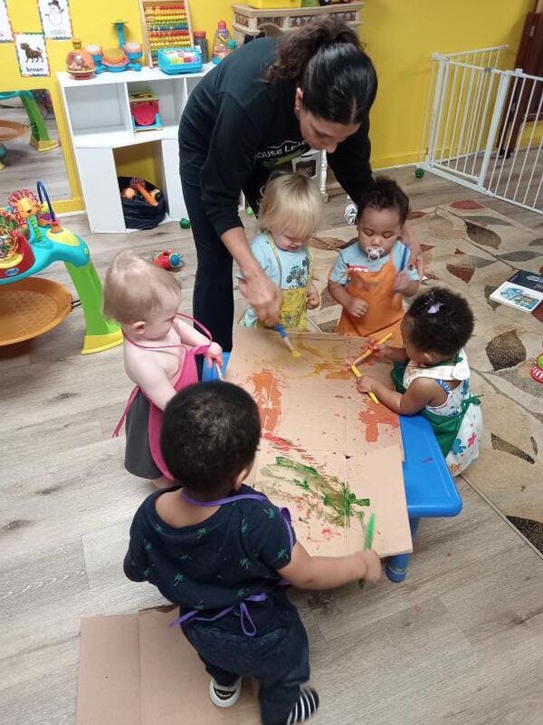 Adult and multiple children painting on a large piece of cardboard