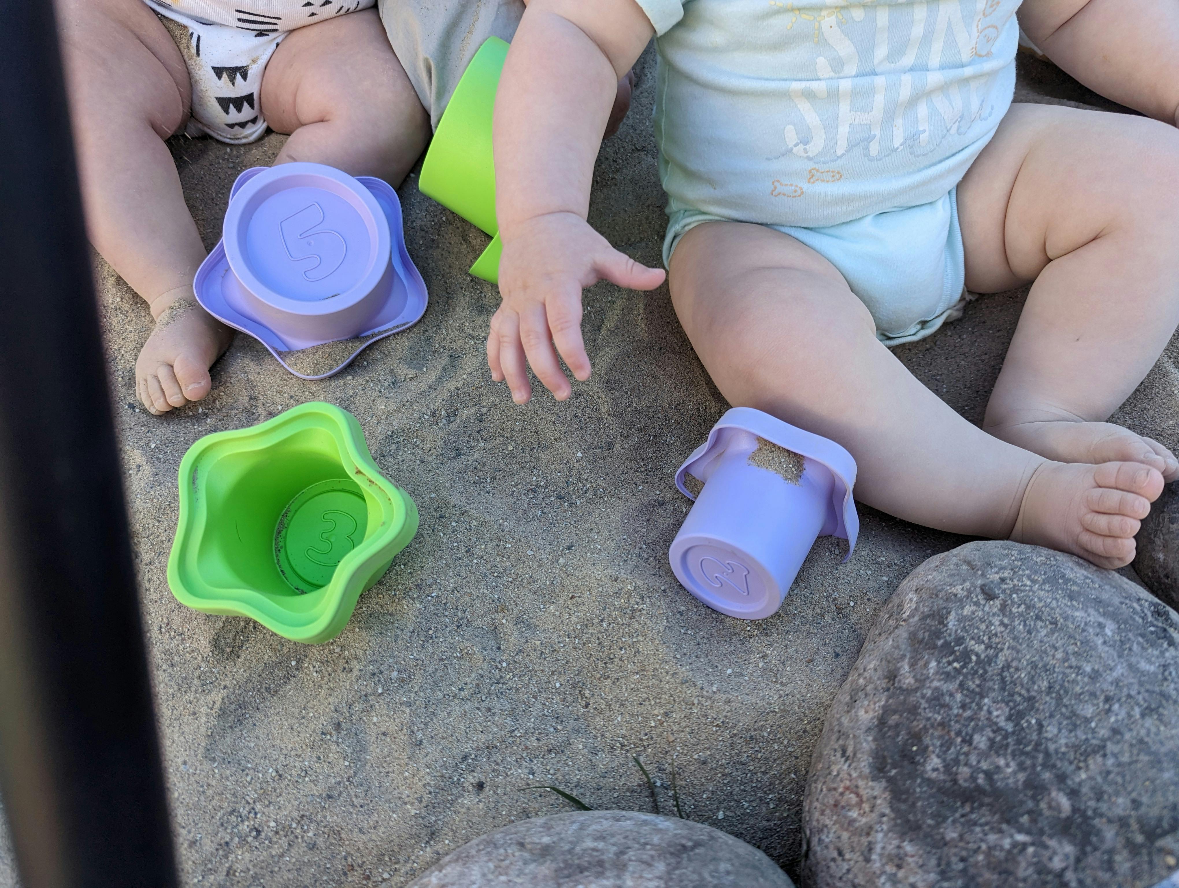 Two babies playing with sand toys in a sandbox