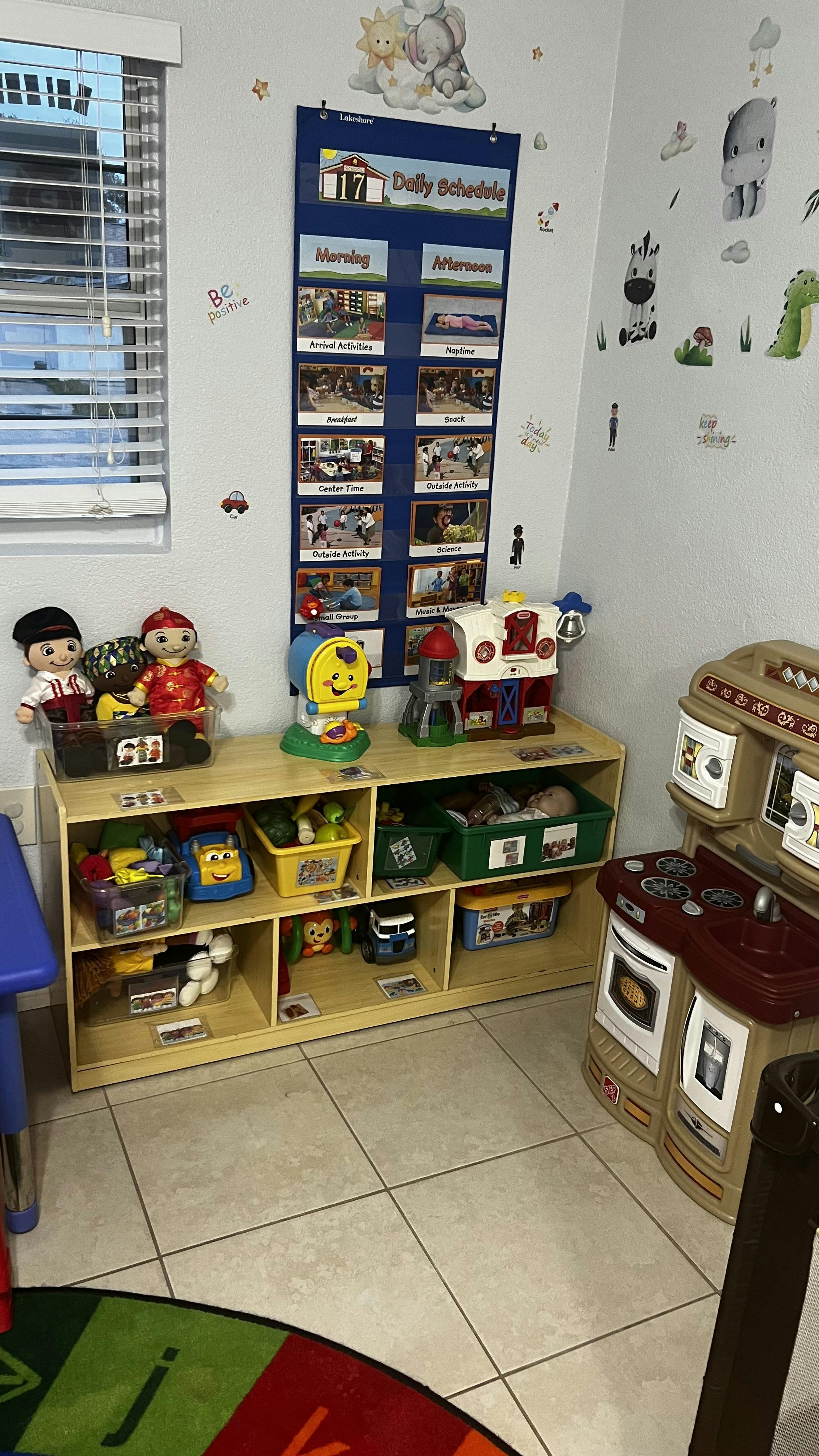 A low shelf with labeled toy bins and a daily schedule chart in a playroom