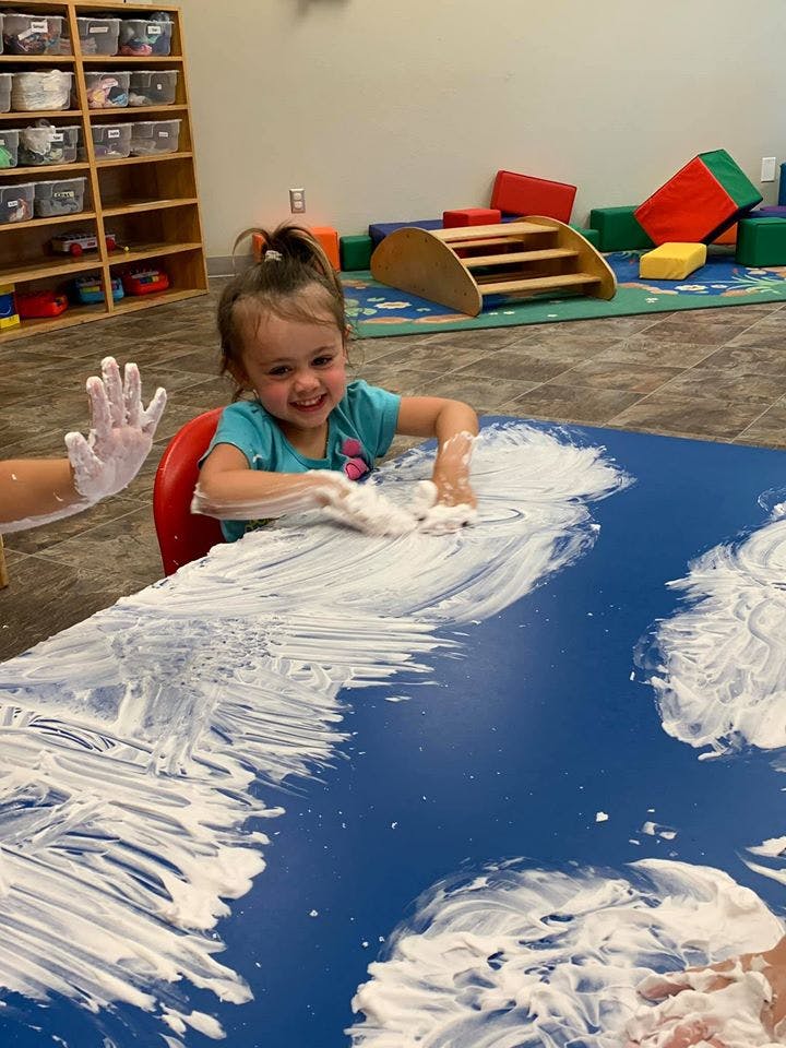 Child playing with shaving cream on a blue table