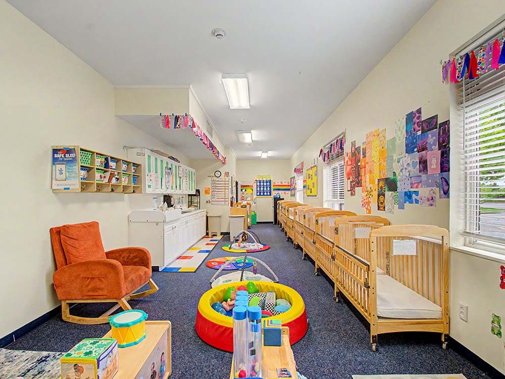 A long room with cribs along one wall and a changing station with storage along the other