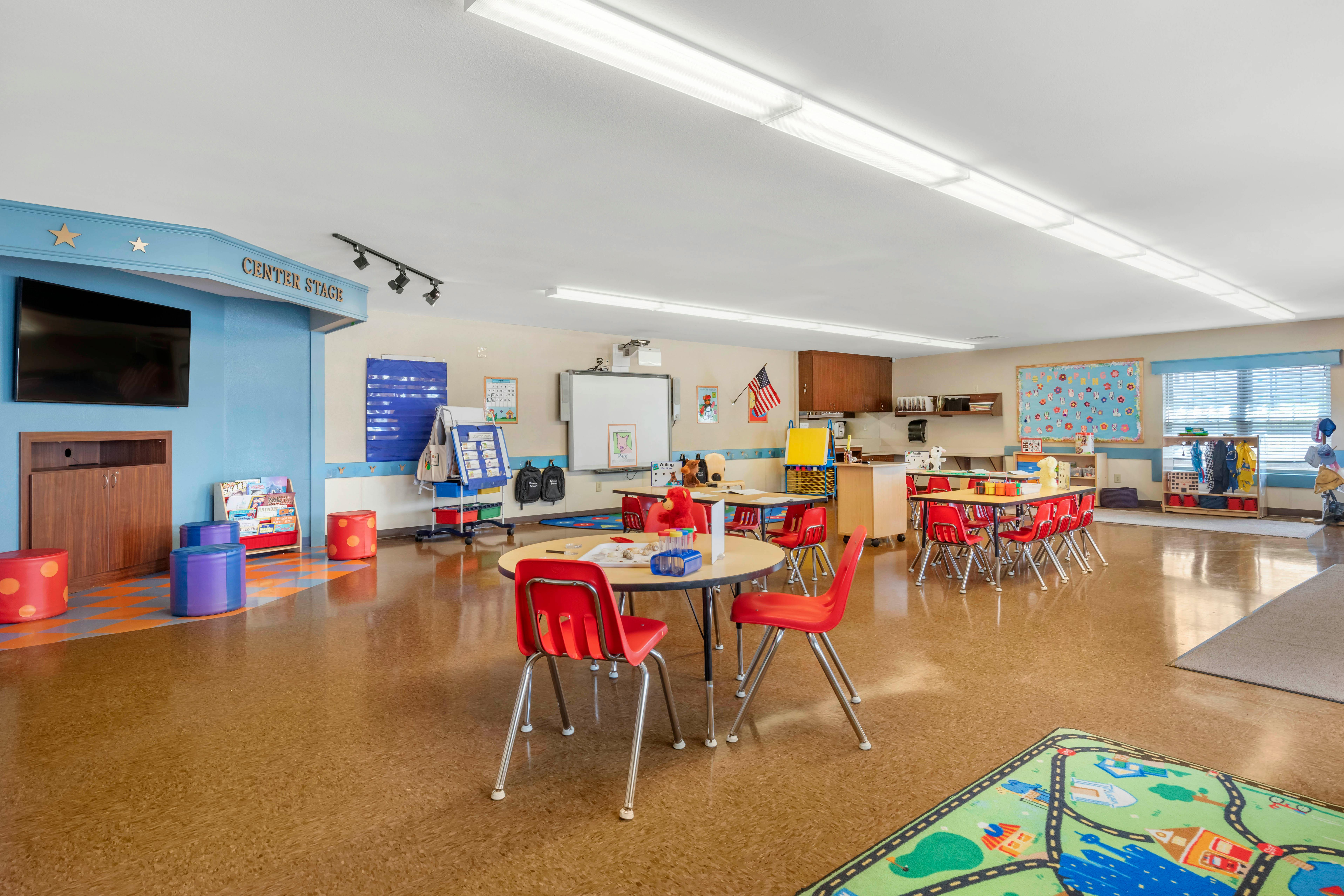 An empty early childhood classroom with small tables and red chairs