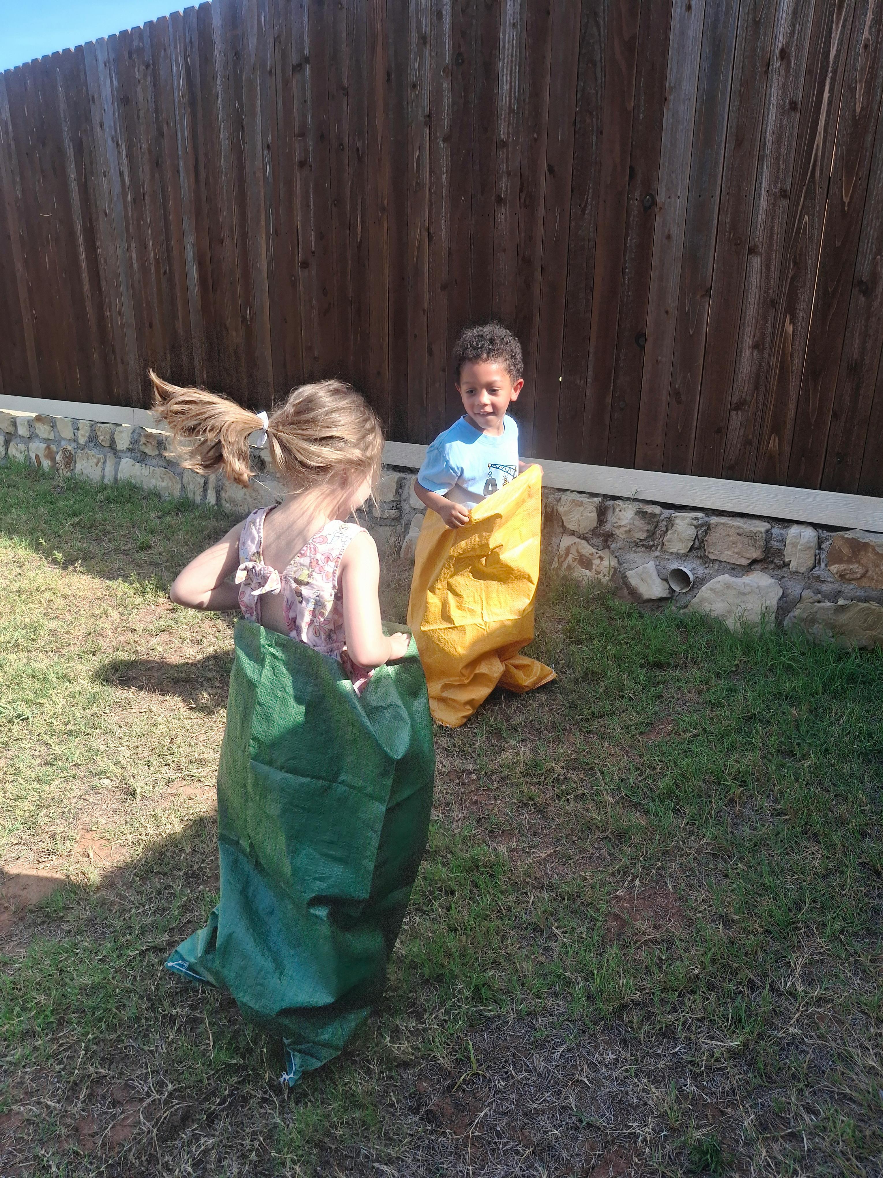 Two children standing in sacks on grass for a sack race