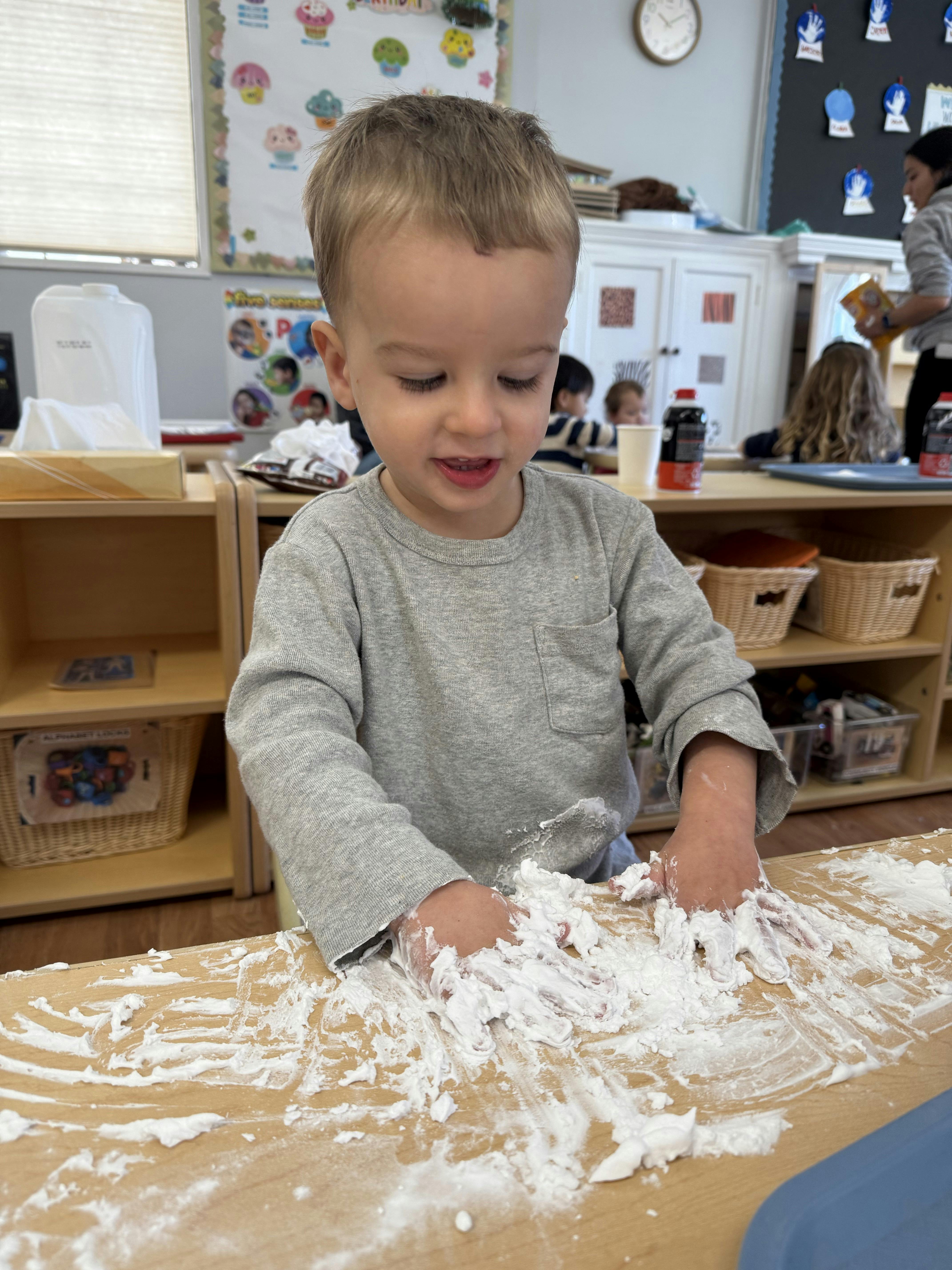 Child playing with white foam on a table in a classroom