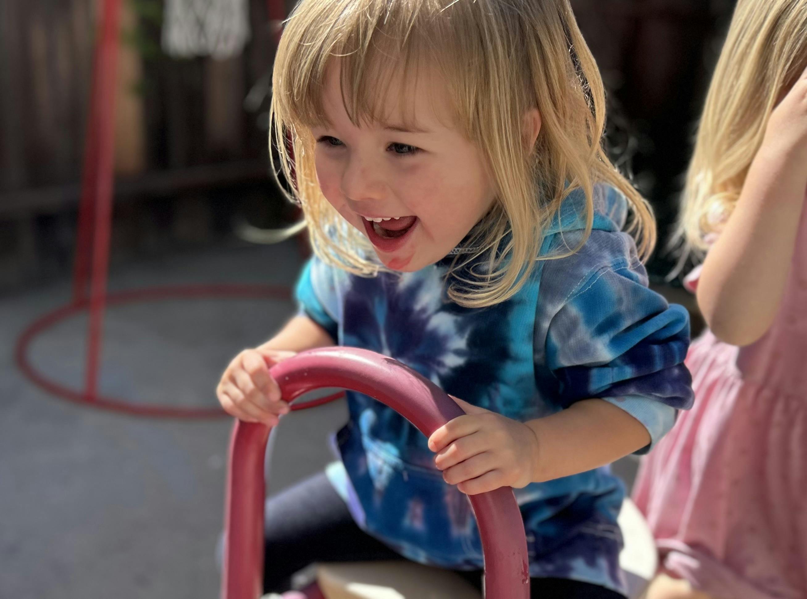 Child with blonde hair in a tie-dye shirt holding a red play bar