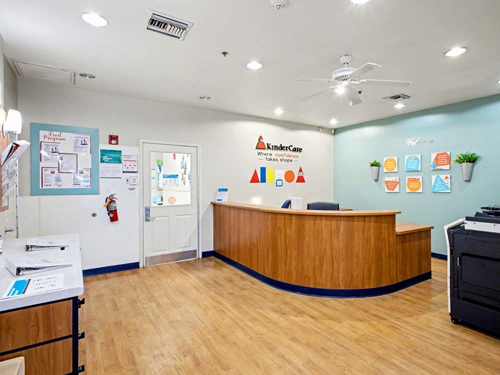 KinderCare reception area with a wooden curved desk, logo, and welcome decor