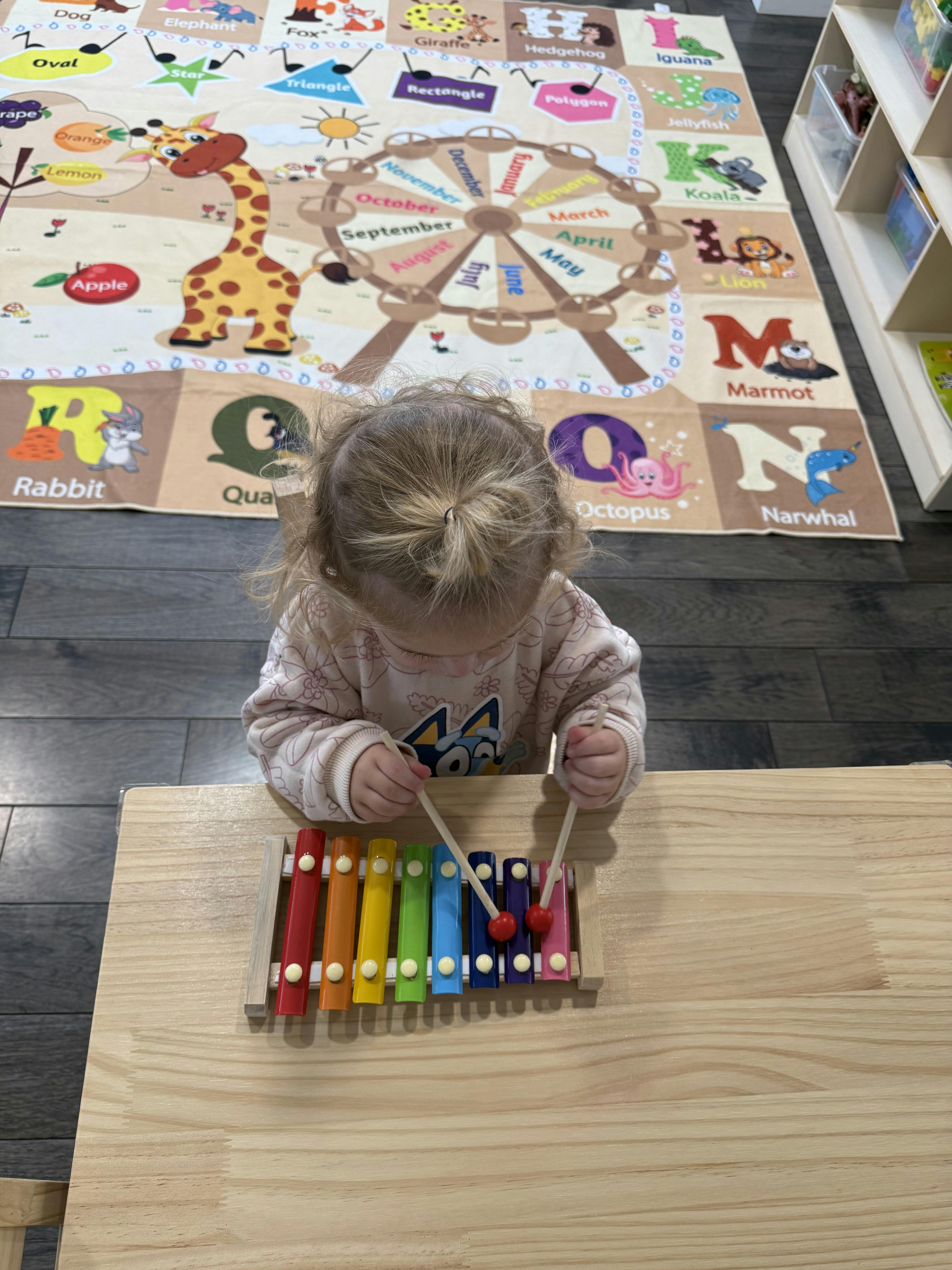 Child playing a rainbow xylophone with mallets