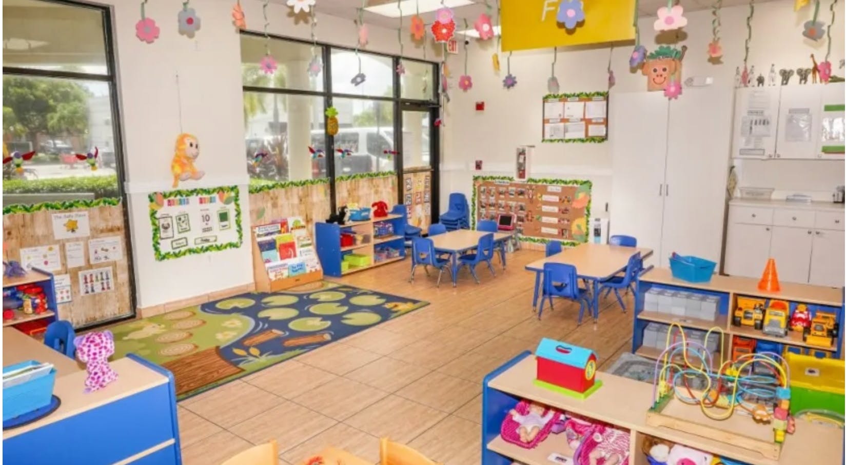 Empty classroom with small tables and chairs, shelves with toys, and decorations