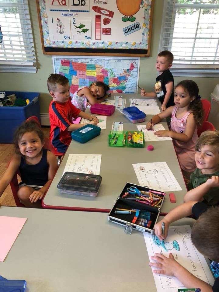 Children sitting at tables in a classroom, drawing and coloring