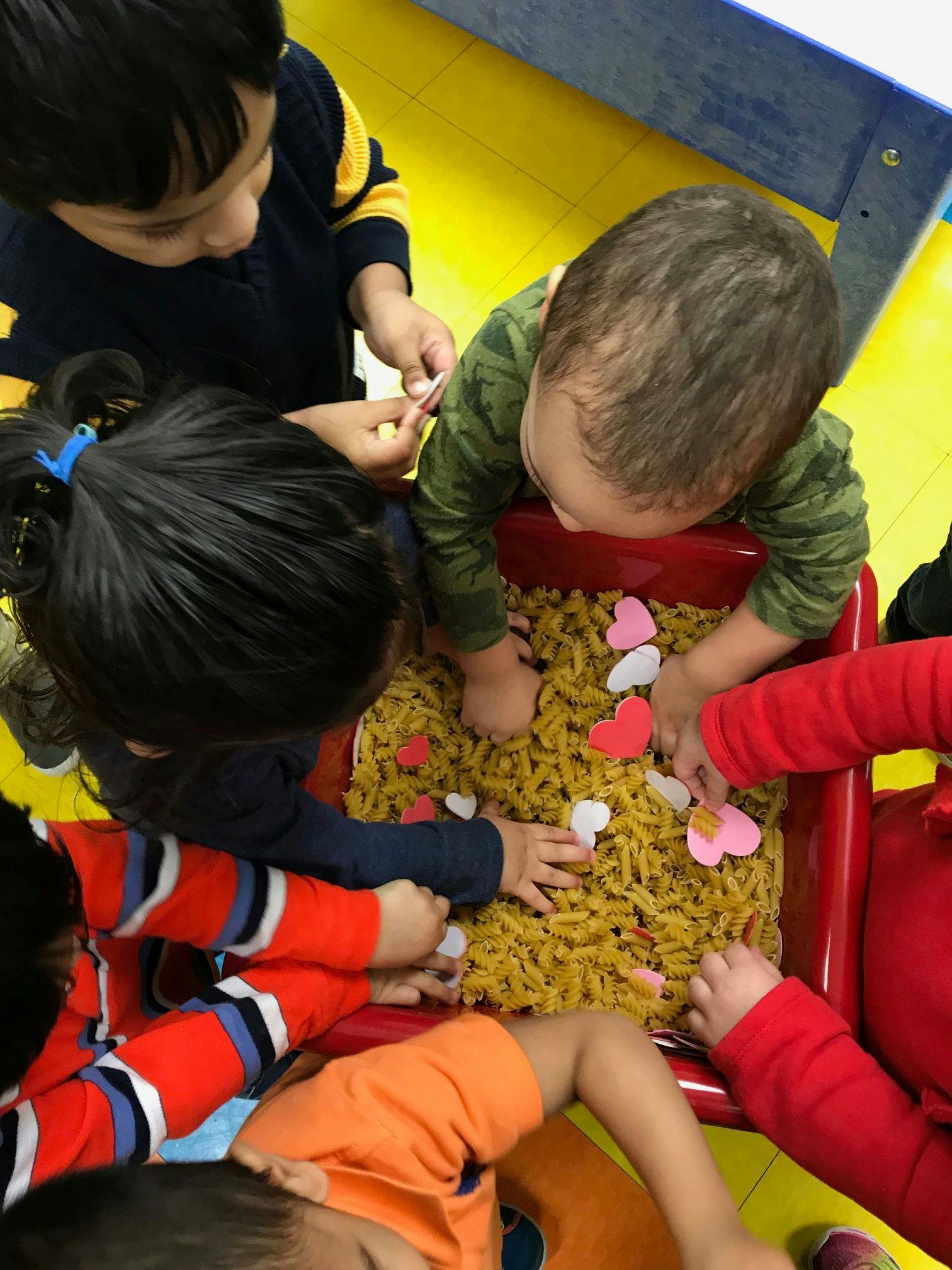 Children playing with pasta and heart shapes in a sensory bin