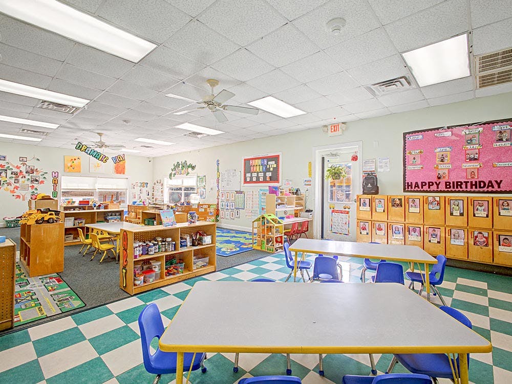 Classroom with small tables and chairs, shelves, and a birthday board