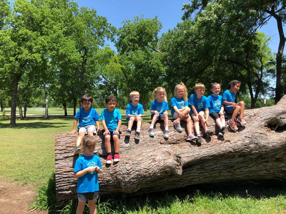Children sitting on a large fallen log outdoors