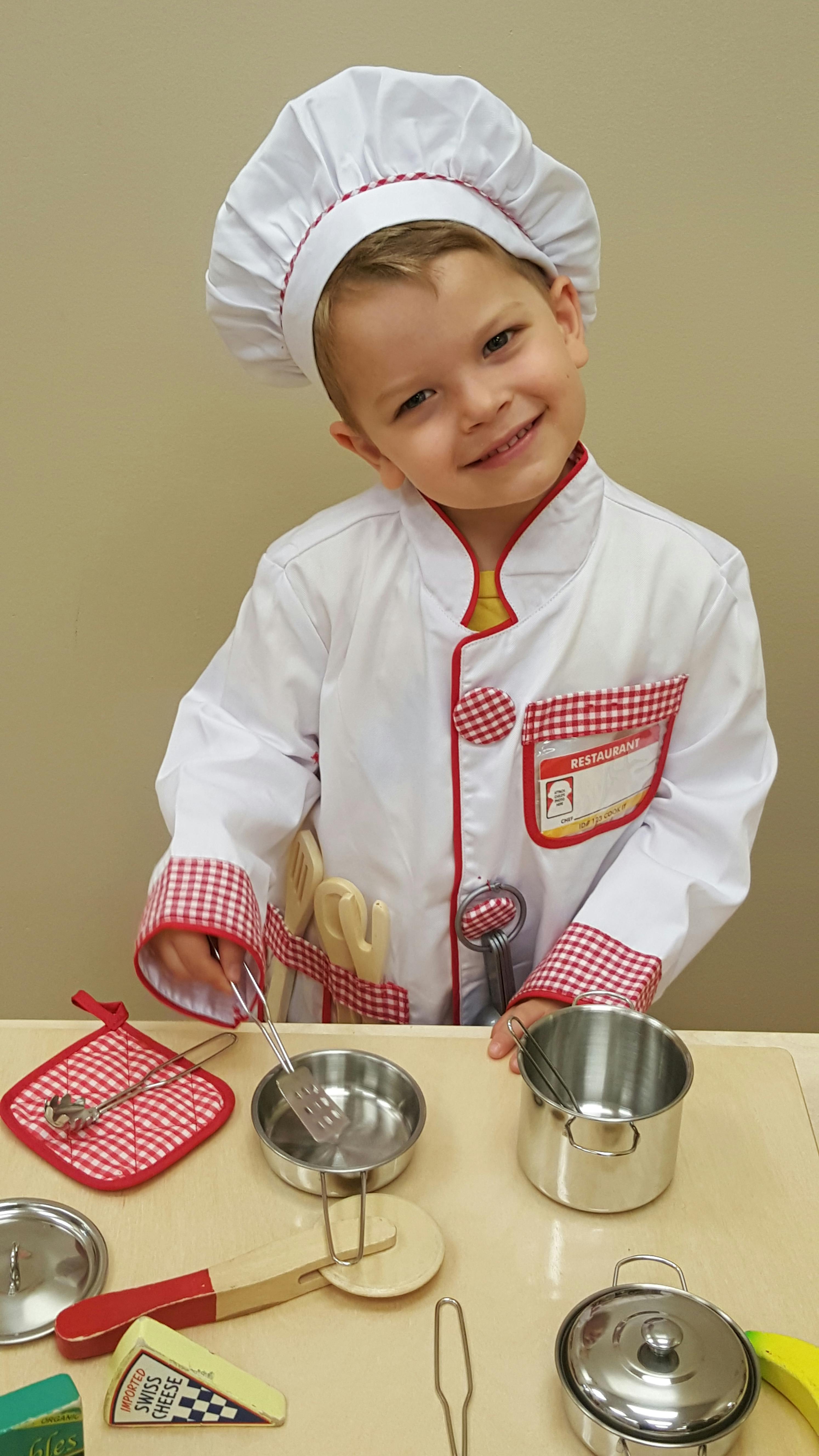 Child in a chef costume playing with toy pots and pans