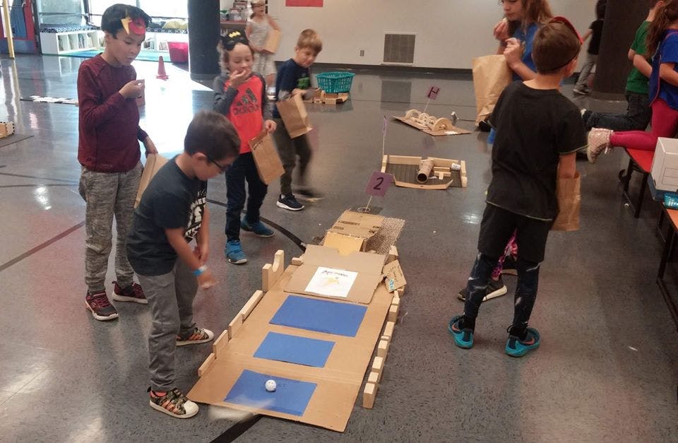 Children playing with a cardboard ramp and a small white ball