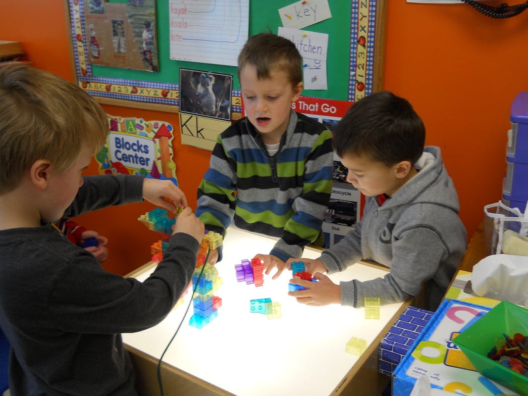Three children playing with colorful blocks on a light table