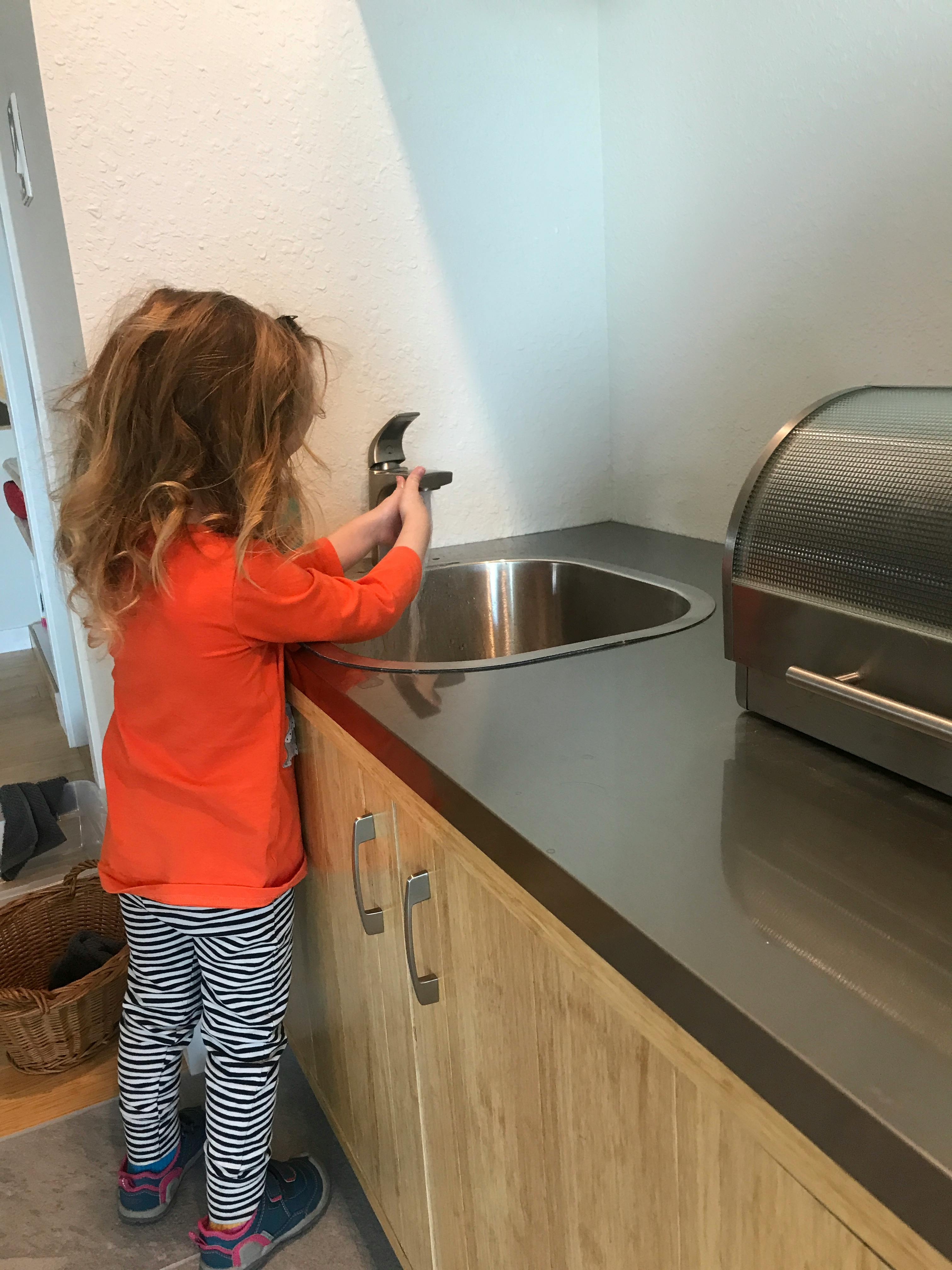 Child standing at a kitchen sink, turning on the faucet