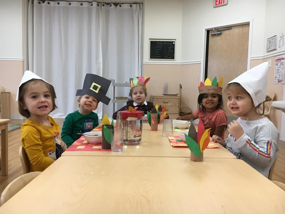 Five children in a classroom wearing paper hats at a table