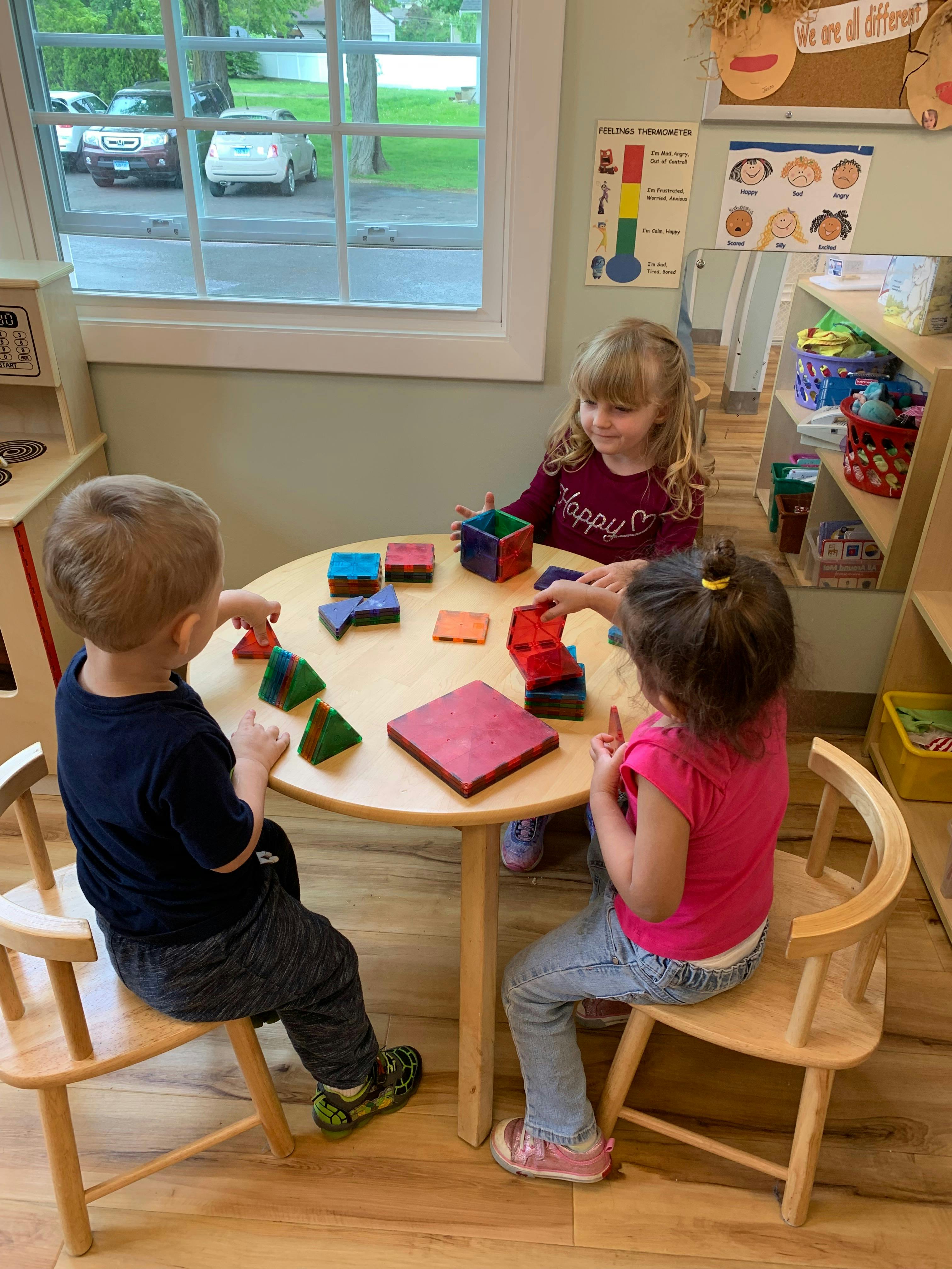 Three children playing with colorful blocks at a small round table