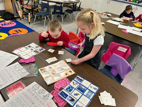 Two children at a table using magnifying glasses and flashcards
