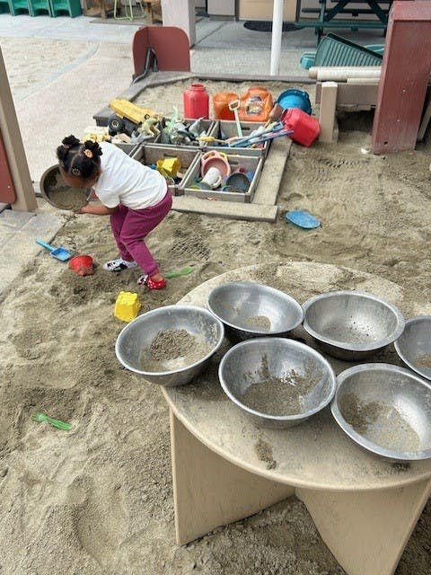 Child playing with sand and metal bowls in a playground