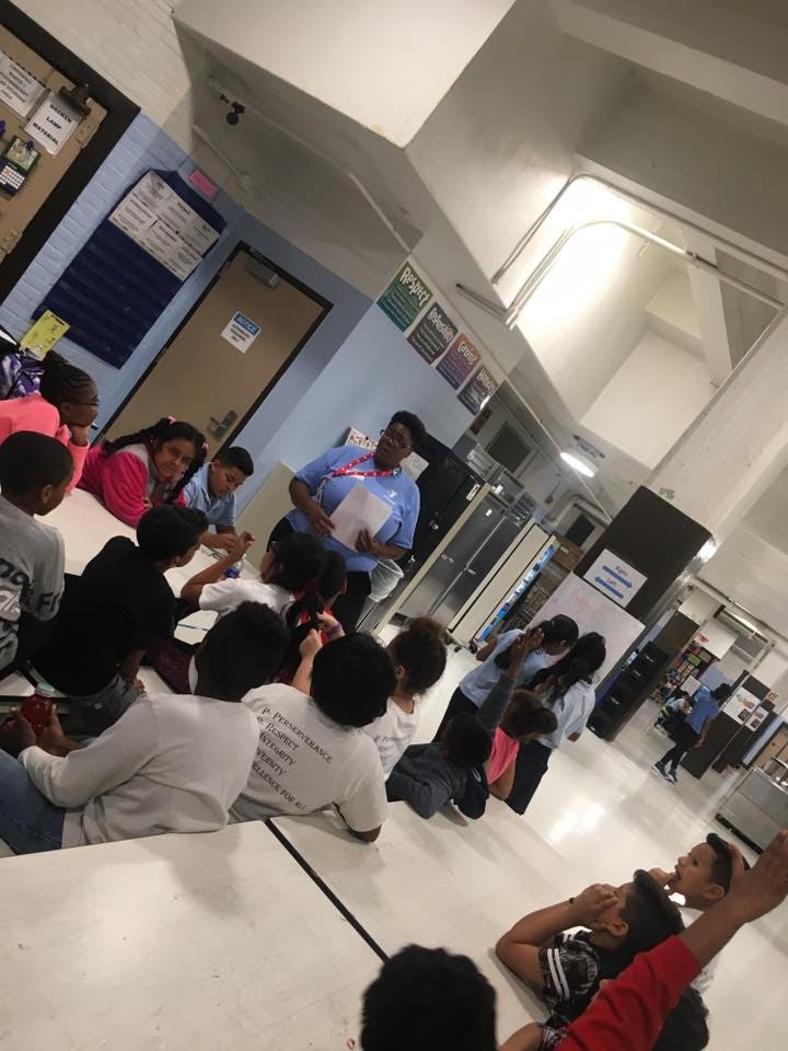 Adult person speaking to a group of children and teens in a hallway