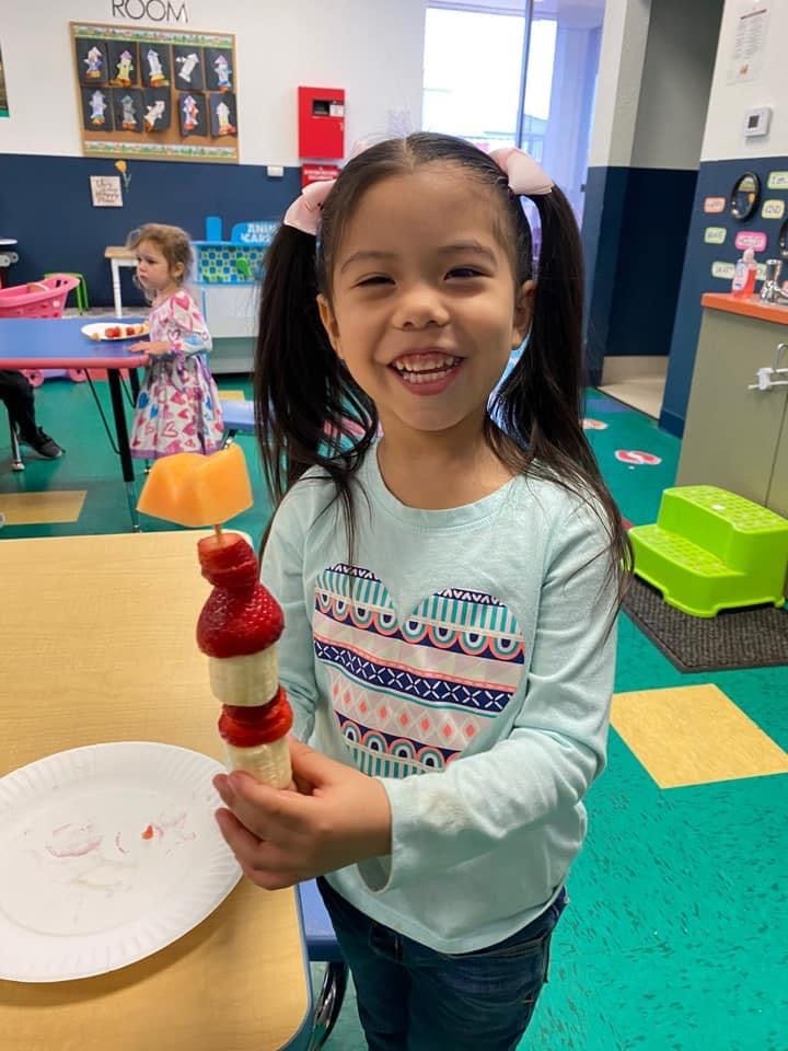Child holding a fruit skewer in a classroom