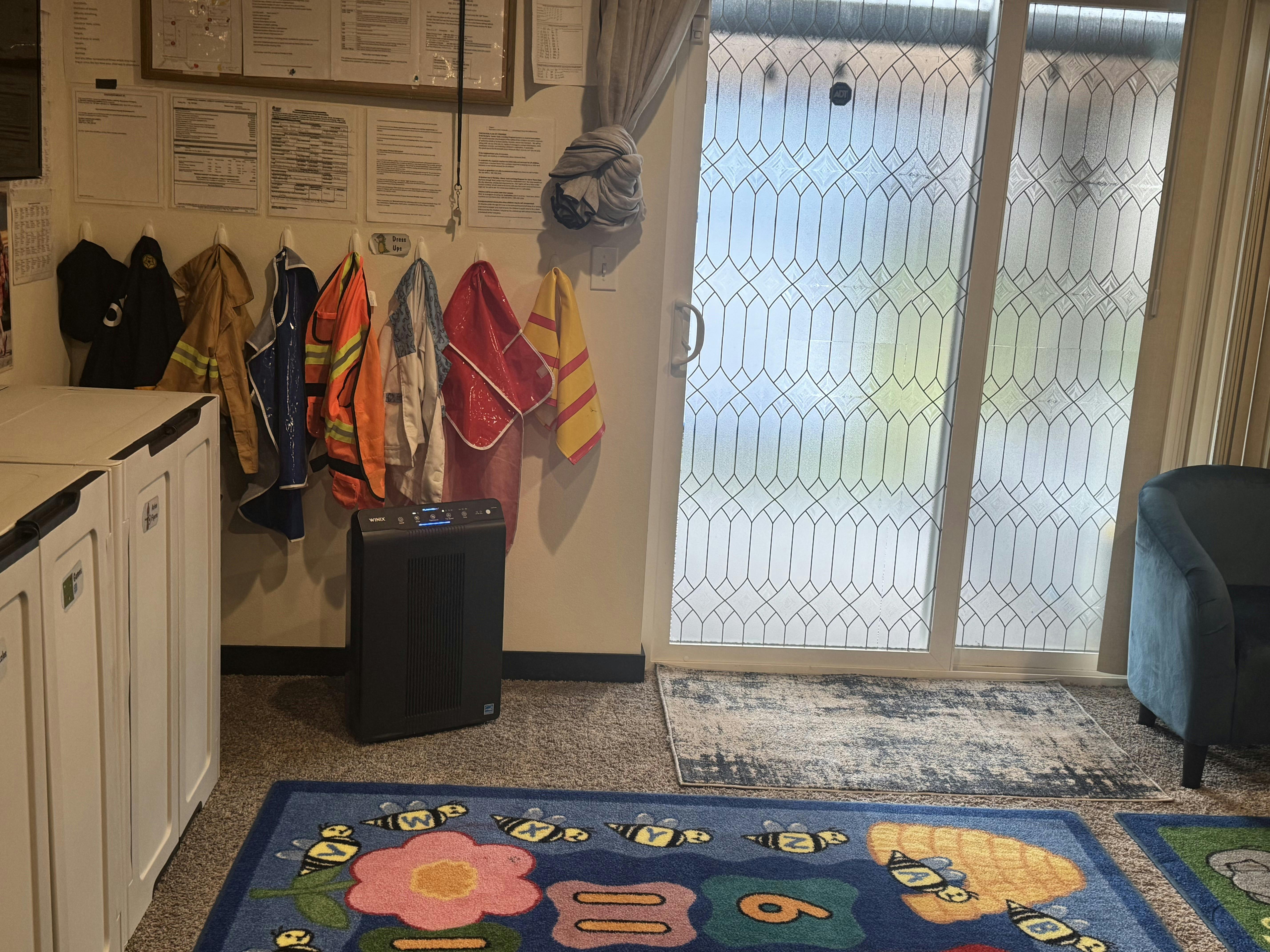 Wall with coats and towels hanging, next to a glass door and a colorful rug