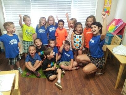 Adult and children posing with arms raised in a classroom