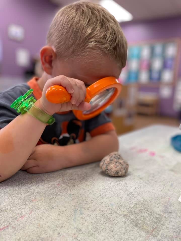 Child looking at a rock with a magnifying glass