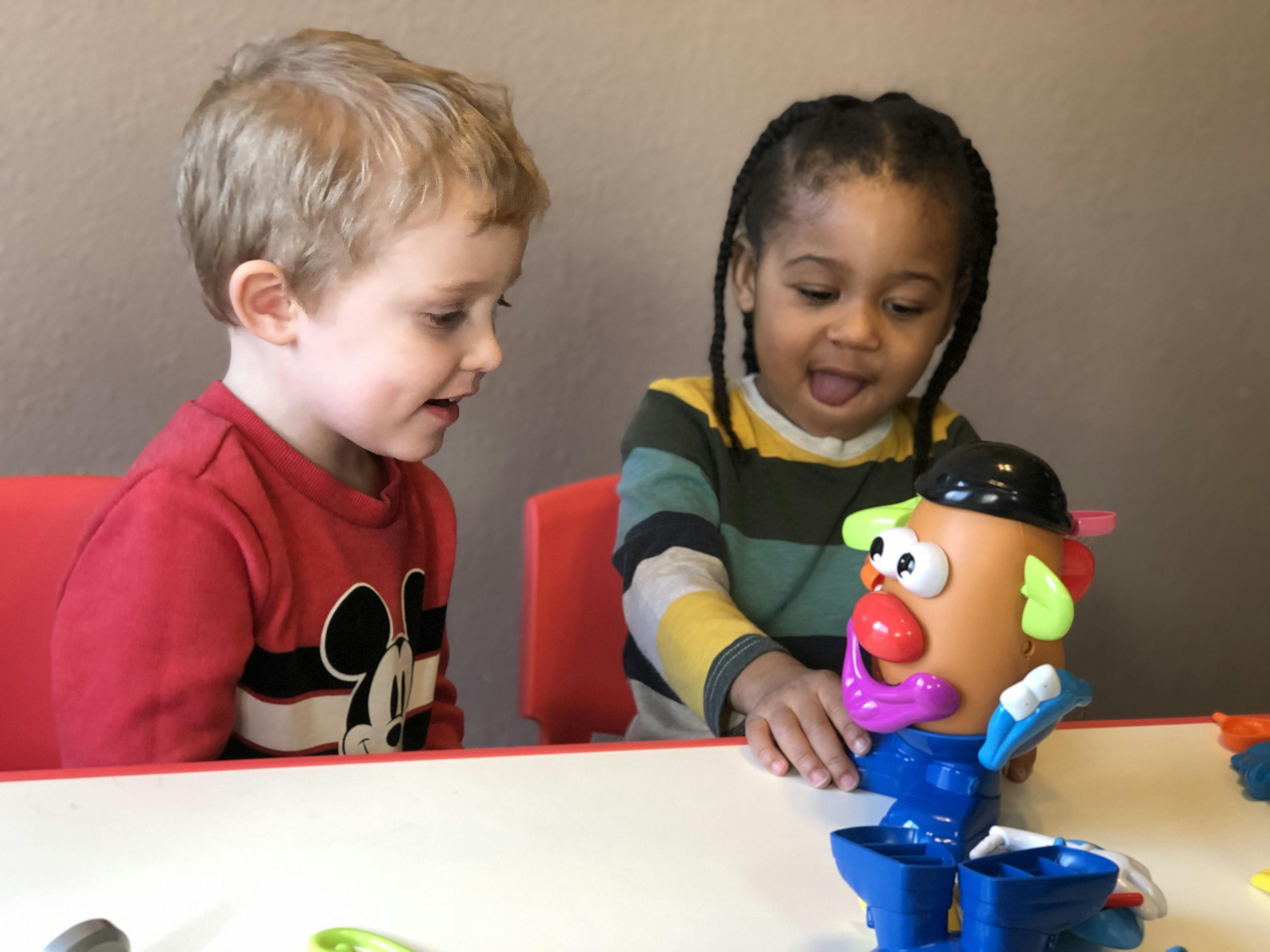 Two children playing with a Mr. Potato Head toy at a table